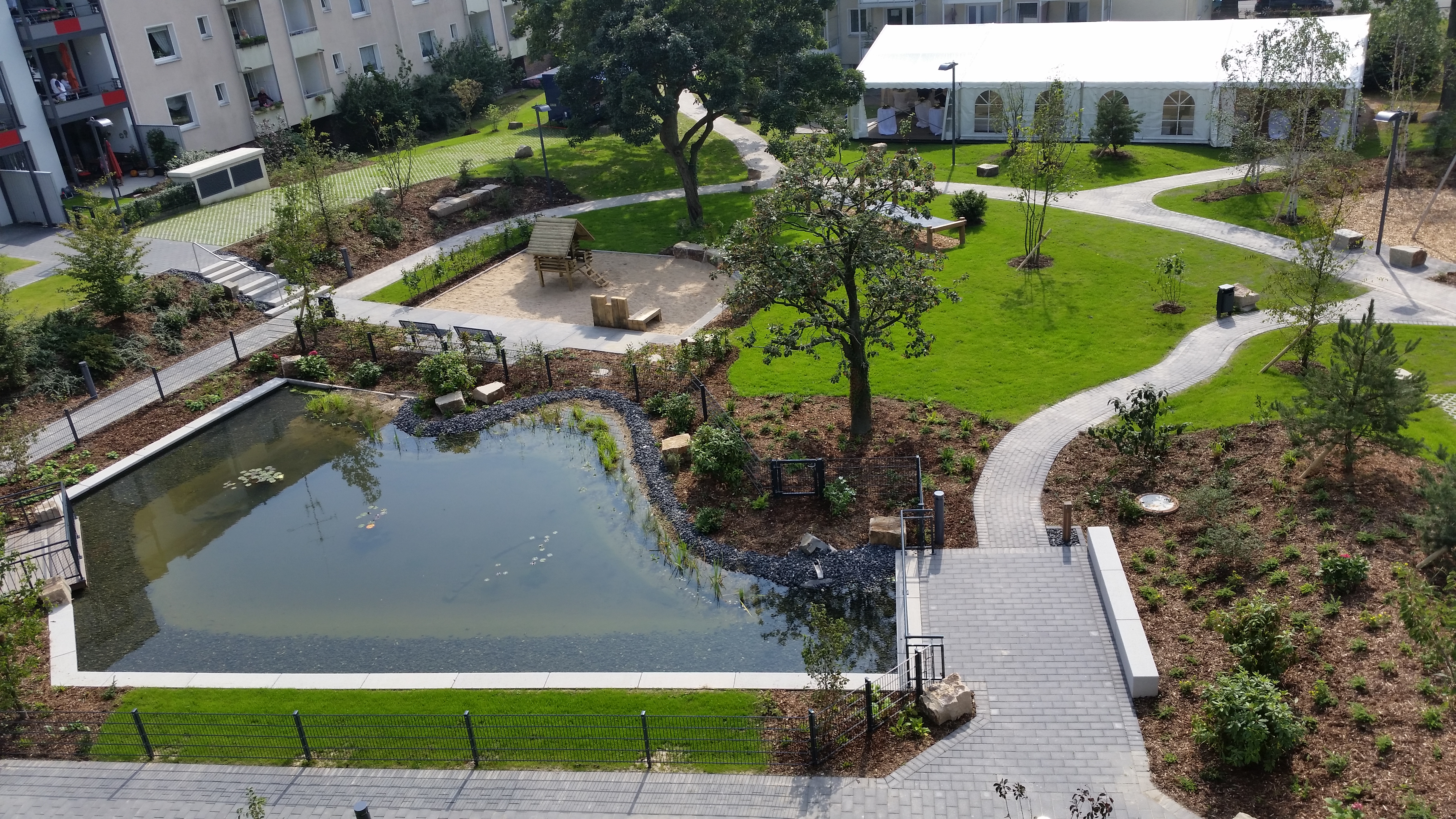 Begrünte Außenanlage mit Teich und geschwungenen Wegen im Wohnquartier