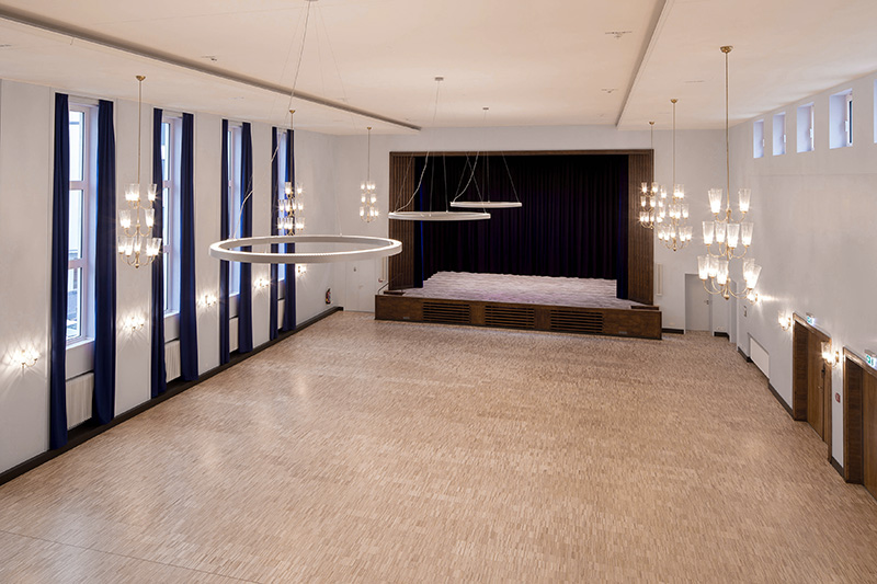 Großzügiger Veranstaltungssaal mit Bühne und hohen Fensterfronten