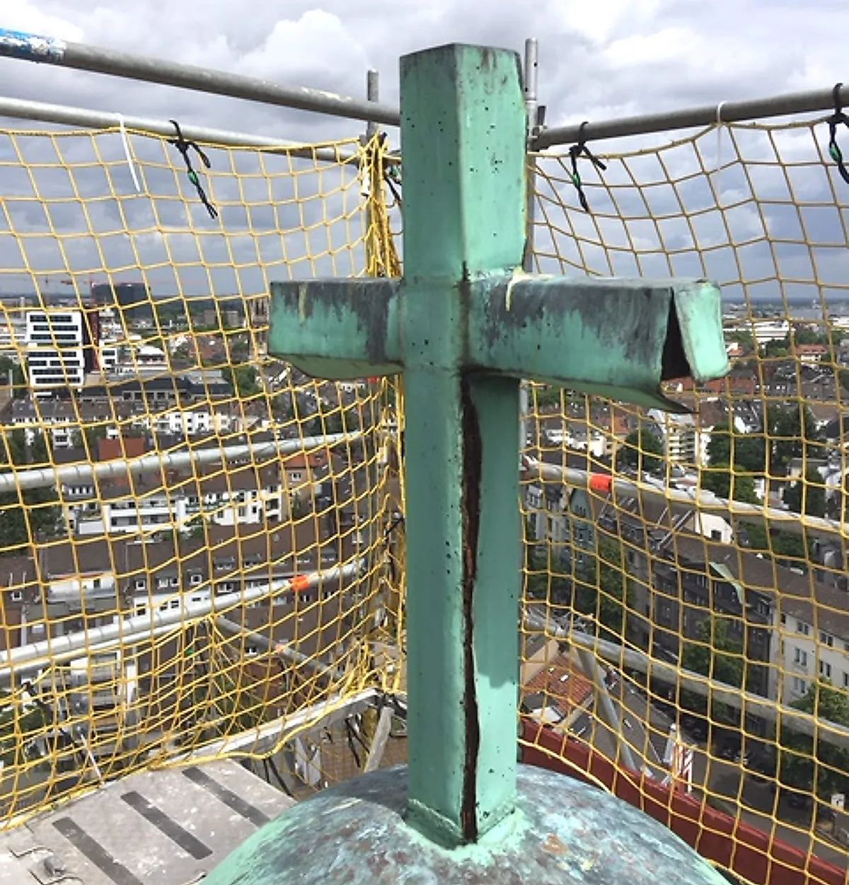 Detailaufnahme eines Turmkreuzes mit Blick über die Stadt