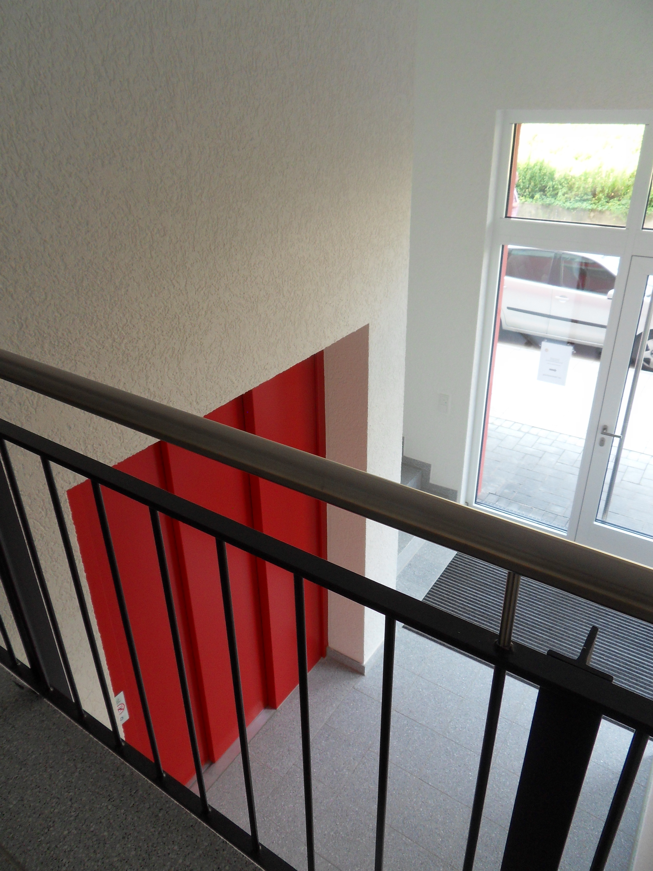 Treppenhaus mit roter Aufzugstür und verglastem Eingangsbereich